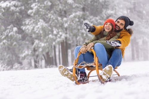 Preview: Couple sitting on sled and sliding down the hill while on winter vacation