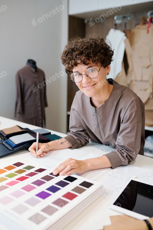 Preview: Young designer making notes and looking through catalogue of textile samples