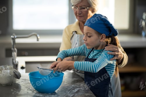 Preview: Grandmother assisting granddaughter to sieve the flour