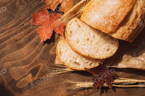 Preview: Sliced fresh loaf of bread in paper packaging with ears of wheat and maple leaves on a wooden table