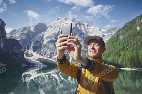 Preview: Smiling young man (tourist) taking selfie against Lake Braies and mountains range of Alps -