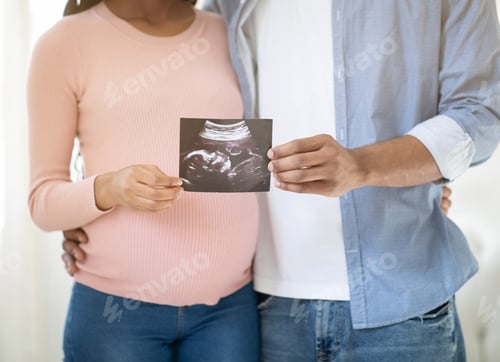 Preview: Cropped view of young pregnant couple holding photo of their unborn baby indoors, close up