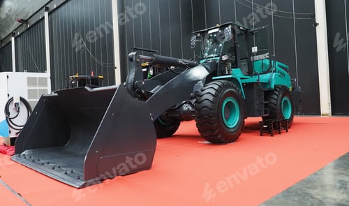 Preview: A large teal and black wheel loader on a red floor mat.