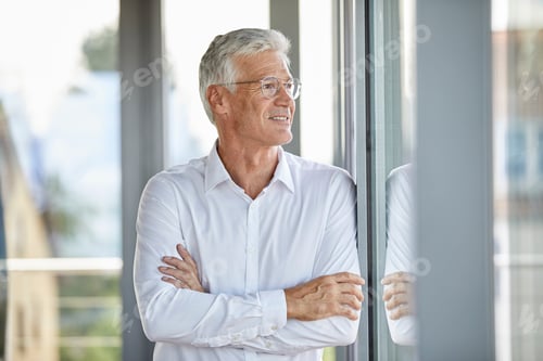 Preview: Businessman in office leaning against window, with arms crossed
