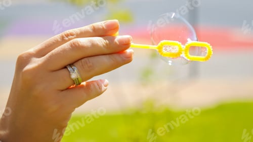 Preview: Closeup of wind blowing soap bubbles at park.
