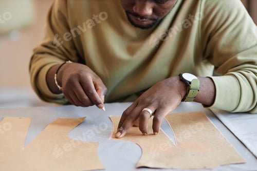 Preview: Hands of young male tailor with piece of chalk contouring sewing patterns
