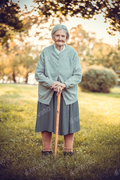 Preview: Senior woman with walking stick in autumn park