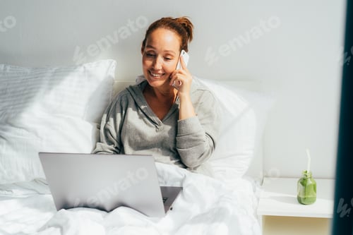 Preview: Woman in Bed Talking on Phone with Laptop