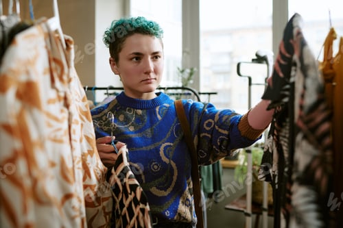 Preview: Young Adult Caucasian Woman Selecting Pre Owned Garments in Urban Thrift Shop