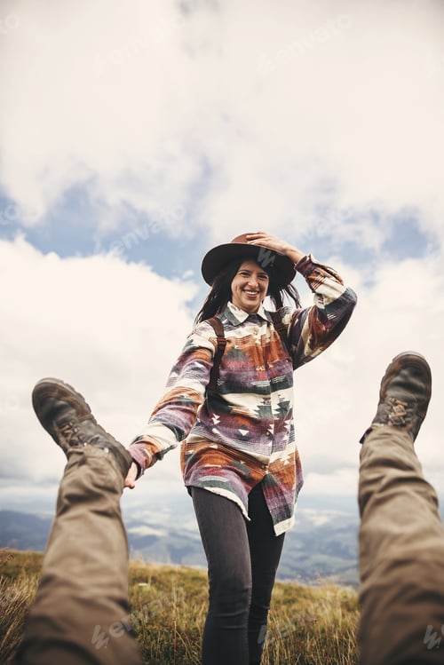 Preview: Stylish hipster girl in hat holding legs of falling man