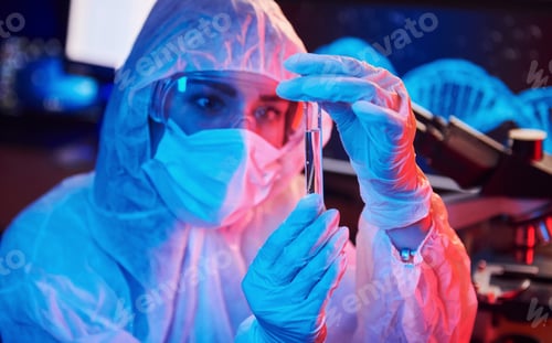 Preview: Nurse in mask and white uniform, holding tube with liquid and sitting in neon lighted laboratory