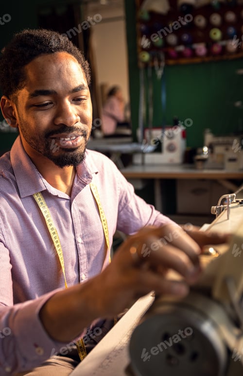 Preview: Male fashion tailor working on the sewing machine for the suit design in his workshop.