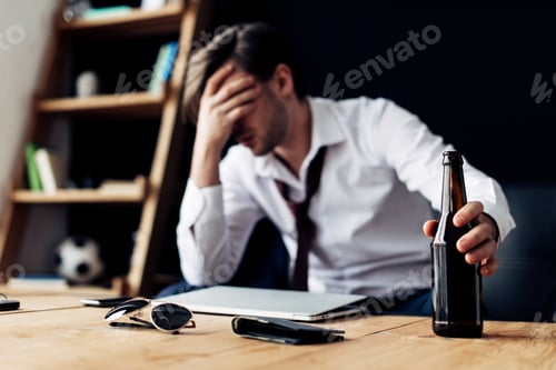 Preview: selective focus of bottle in hand of man having headache after party