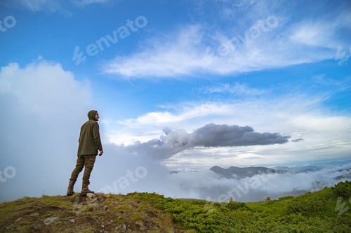 Preview: The man standing on the mountain on the white clouds background.