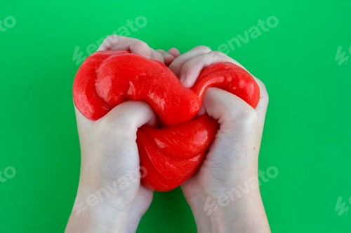 Preview: Bright red slime in children's hands on green background. Education, creativity, childhood concept.