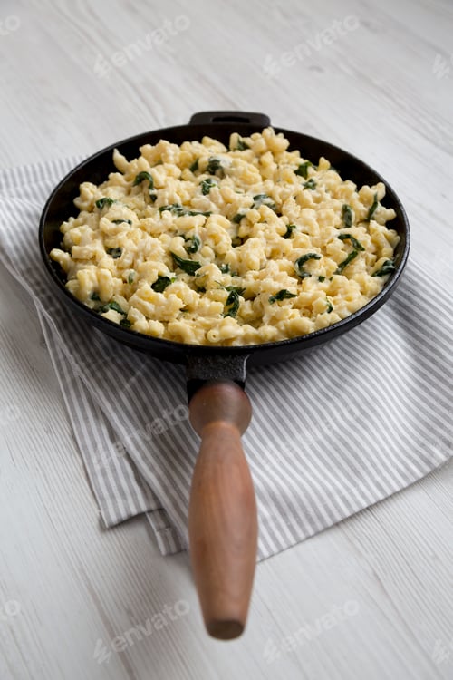 Preview: Homemade Spinach Mac and Cheese in a cast-iron pan on a white wooden background, side view.