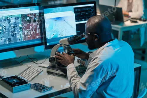 Preview: African scientist with microscope working in front of computer monitors