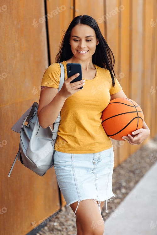 Preview: Smiling Woman with Basketball Using Mobile Phone Outdoors
