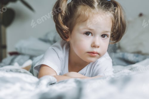 Preview: Little dark-haired girl 2-4 with two ponytails lies on bed on her stomach looking into frame