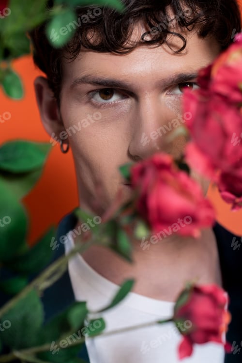 Preview: Portrait of young man looking at camera near blurred roses on orange background