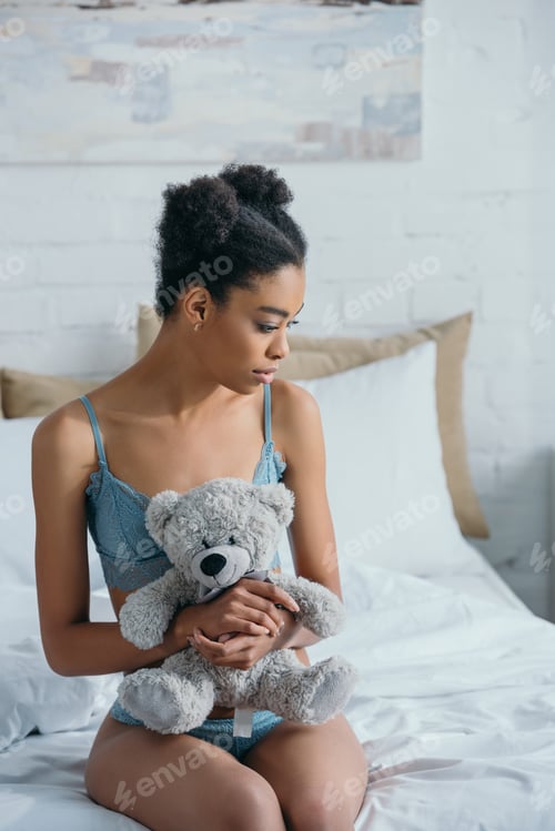 Preview: beautiful african american girl with teddy bear sitting on bed in morning