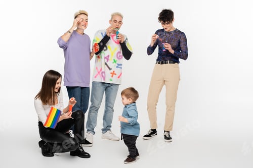 Preview: happy lesbian woman with rainbow flag near toddler boy and lgbtq community friends on grey