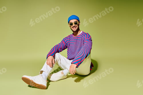 Preview: Young man showcases vibrant fashion style in trendy outfit against green backdrop