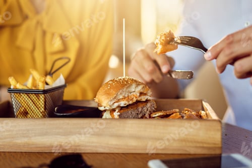 Preview: Close-up of man eating cheeseburger on a lunch with his girlfriend.