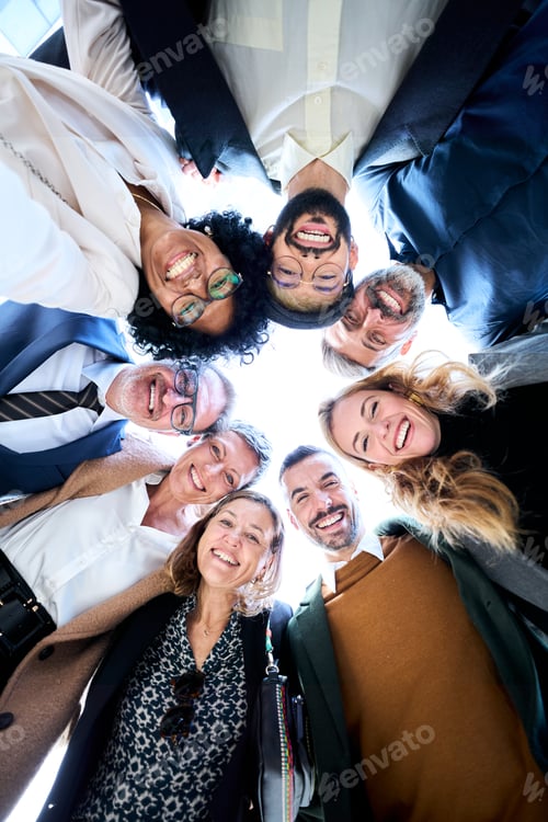 Preview: A group of diverse business people in formal wear gathered in a circle smiling and stacking hands