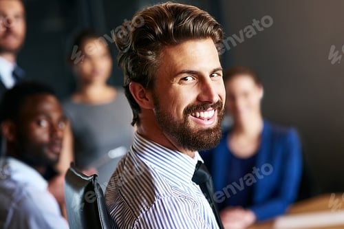 Preview: Portrait of a smiling businessman sitting in an office with colleagues in the background