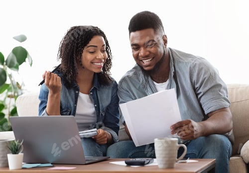 Preview: Black couple reading financial documentation at home while planning family budget