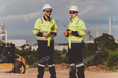 Preview: Two engineers discussing project updates at a construction site with refinery backdrop