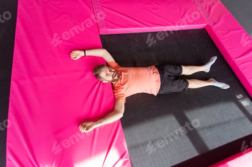 Preview: Fitness, fun, leisure and sport activity concept - Man lying on a trampoline indoors, top view