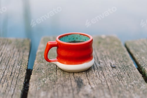 Preview: Woman holds cup of coffee on wooden pier on lake