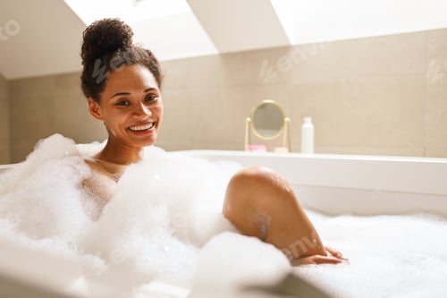 Preview: A woman smiles with comfort while bathing in a foamy bathtub