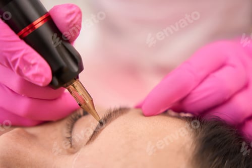 Preview: Master in pink protective gloves makes a tattoo of eyebrows