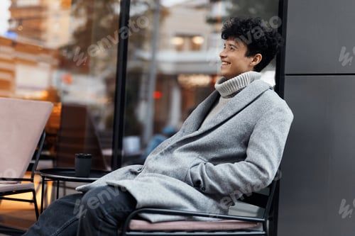 Preview: Fashion man in gray coat sitting with woman on chairs outside coffee shop