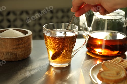Preview: Woman stirring tea with spoon at dark table, closeup