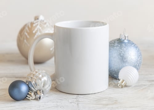 Preview: White blank coffee mug near cream and light blue Christmas baubles closeup, mockup