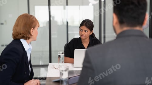 Preview: businesspeople discussing papers and working on laptops.
