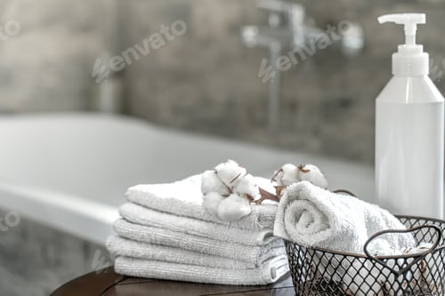 Preview: Stack of clean white bath towels and body care product close up.