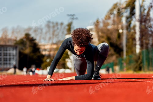 Preview: Young woman stretching her muscles before running on sport track outdoors.