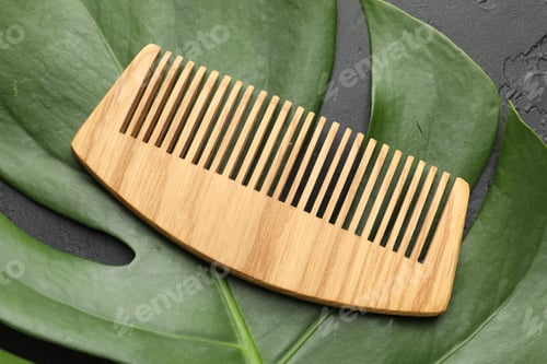 Preview: Wooden comb and monstera leaf on dark textured table, top view