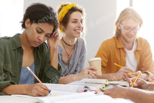 Preview: Mixed-race college female student having conentrated look in her notebook writing something with pen