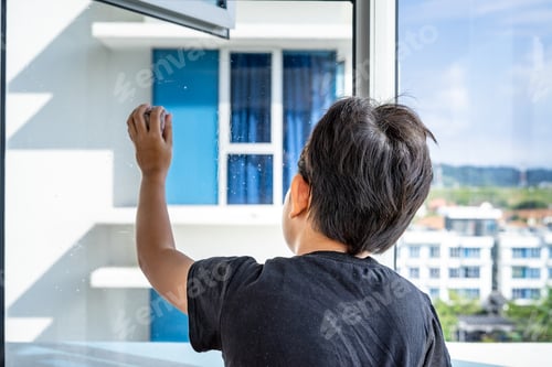 Preview: Young boy standing alone looking out of the window in an apartment during coronavirus pandemic.