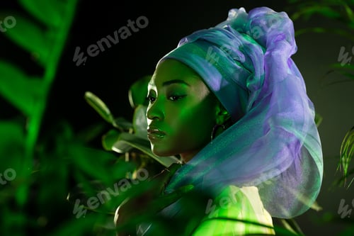 Preview: attractive african american woman in wire head wrap under green light behind leaves