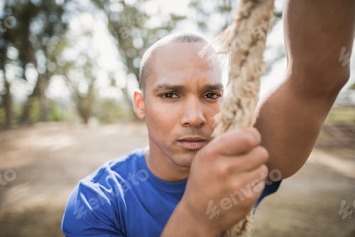 Preview: Portrait of fit man climbing rope during obstacle course