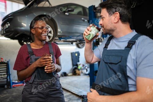 Preview: Two happy mechanics drinking coffee during break in auto repair shop