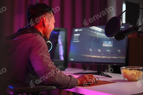 Preview: Side view shot man streamer playing online video game on personal computer in neon room.