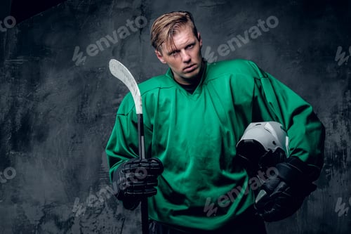 Preview: Hockey player holds protective helmet and playing stick on grey